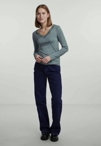 Top de manga longa em teal com decote em formato de ondas, combinado com calças largas de um azul escuro. O conjunto apresenta um tecido suave e macio, com um corte descontraído.