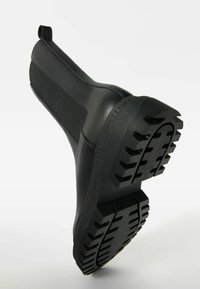 Botas de tobillo de goma negra con una superficie texturizada, paneles laterales elásticos y una suela resistente para mejorar la tracción y el agarre.