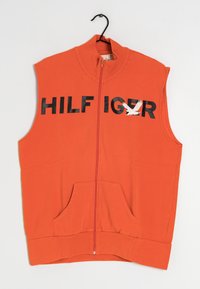 Orange ärmlös zip-up väst med svarta texten "HILF IG R" och en vit örn grafik, framfickor samt ribbad krage och nederkant.