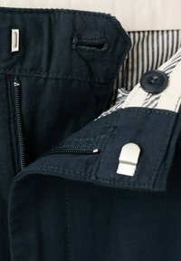 Mørke marineblå bukser, taljebånd med lynlås, metal krog-og-bjælke lukning, knap og stribet indvendigt foring synlig.