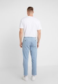 Ljusblå randiga kordbyxor med avslappnad passform, utrustade med två bakfickor och bälteshällor, i kombination med en vit t-shirt och vita sneakers.