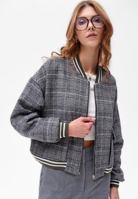 Szaro-czarna bomberka w kratę z zielonymi i białymi prążkowanymi mankietami oraz kołnierzem; posiada zamek błyskawiczny oraz boczne kieszenie.