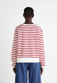 Sweatshirt a righe rosse e bianche con polsini a costine, scollatura arrotondata e tessuto morbido. Abbinato a pantaloni in denim blu larghi.