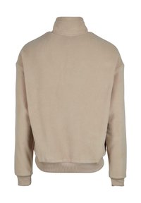 Beige fleece genser med høy krage, senkede skuldre og ribbede mansjetter og nederkant. Glatt tekstur, avslappet passform og ensfarget.