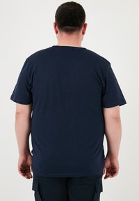 Tricou bleu marin cu mânecă scurtă, cu decolteu rotund, fabricat dintr-un material moale, având un tiv drept și un etichetă pe cusătura laterală stângă.