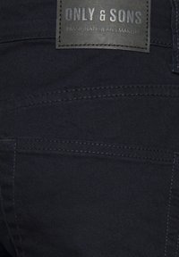 Mørke denimjeans med subtil søm, med et rektangulært lærmerke merket "ONLY & SONS" og teksturert overflate.