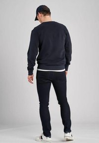 Marinblå sweatshirt med ribbade muddar och nederkant, ihopparat med mörka jeans och vita sneakers. Kapsyl kompletterar den avslappnade stilen.