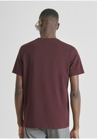 Camiseta de manga corta burdeos con cuello redondo; fabricada en algodón; textura suave, color sólido y diseño sencillo. Vista trasera únicamente.