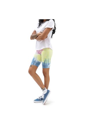 Osoba ubrana w białą koszulkę Vans, kolorowe (tie-dye) żółto-niebieskie spodenki kolarskie, białe skarpetki Vans oraz niebieskie trampki Vans, stoi z założonymi ramionami.