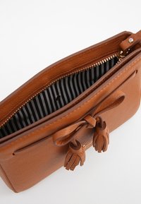 Ruskea nahkainen käsilaukku vetoketjulla, jossa raidallinen sisusta ja koristeelliset hapsut ulkopuolella. Sileä pinta.