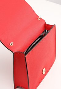 Borsa sintetica rossa con finitura testurizzata, accenti neri, chiusura a scatto magnetico e tasca interna a strisce bianche e nere.
