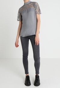 Top de encaje y tela gris con cuello alto, mangas cortas, combinado con jeans ajustados grises y zapatillas de plataforma negras.