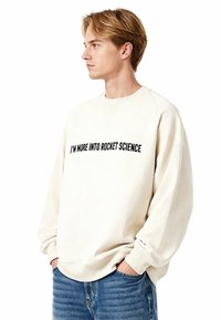 Roomkleurige sweatshirt met een losse pasvorm, met een zwarte gedrukte quote "I'M MORE INTO ROCKET SCIENCE" aan de voorkant.