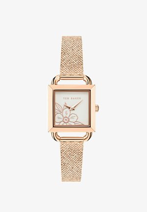 Roza zlata kvadratna ura z teksturiranim kovinskim trakom. Bela številčnica z cvetličnim vzorcem in zlatimi detajli. Ime blagovne znamke "Ted Baker" je prikazano.
