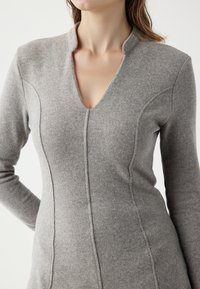 Grijze gebreide trui met een V-hals, lange mouwen en een getailleerd silhouet. Het heeft verticale naden en een zachte textuur.