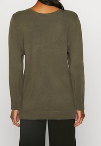 Oliivinvihreä neulepaita, pehmeä tekstuuri, pitkät hihat, resorit hihansuissa ja helmassa, pyöreä pääntie. Päällä mustat housut, takaa katsottuna.