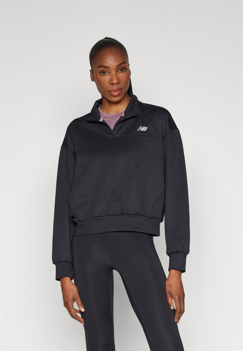 Felpa nera con zip e colletto alto, con orlo a costine, rifinita con un logo sul petto. Indossata con leggings neri abbinati.