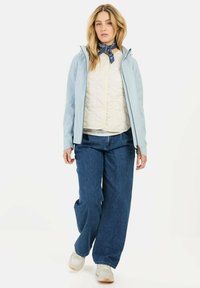 Lysblå vandtæt jakke, vatteret cremefarvet inderlag, afslappede blå jeans, hvide sneakers med tan-detaljer og et mørkeblåt mønstret tørklæde.