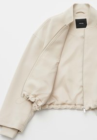 Beige bomber jacket with a soft texture, ribbed cuffs, and a zip closure. Features elasticized hem and interior label.