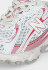 Λευκό και ροζ αθλητικό παπούτσι New Balance με πλεκτό ύφασμα, λευκά κορδόνια και υφασμένο πάτο, εμφανιζόμενο σε κοντινή λεπτομέρεια.