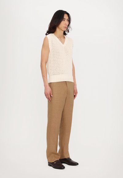 Top sans manches en tricot crème avec un col en V, associé à un pantalon en lin beige ample et des mocassins foncés avec un accent de boucle.