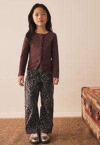 Cardigan bordeaux à manches longues avec boutons, associé à un jean large gris à imprimé léopard et des baskets métalliques. Tenue simple et décontractée.