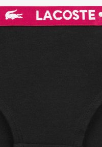 Juodi medvilniniai apatinių drabužių kelnaitės su rausva juostele, ant kurios parašyta „LACOSTE“, pasižyminčios lygiu paviršiumi ir paprastu dizainu.