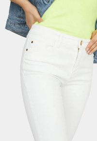 Jeans blancos ajustados, con cremallera, cierre de botón metálico y dos bolsillos frontales con sutiles acentos dorados.