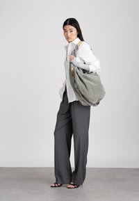 Kvinna i vit skjorta och grå vida byxor bär en stor grå suède axelväska med gulddetaljer.