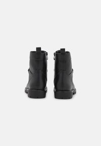 Botas de tobillo de cuero negro con una textura suave, suela de goma resistente, cuello alto y tiradores dobles en la parte trasera para facilitar su uso.