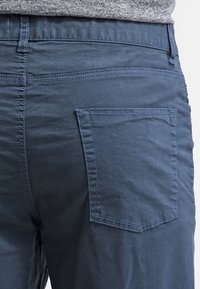 Donkerblauwe katoenen broek met een achterzak, voorzien van een enkel gestikt ontwerp en een gladde, licht gestructureerde stofoppervlak.