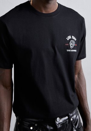 Czarny bawełniany t-shirt z nadrukiem czaszki, krótkie rękawy, okrągły dekolt i luźny krój. W zestawie ze spodniami skórzanymi w kolorze czarnym.