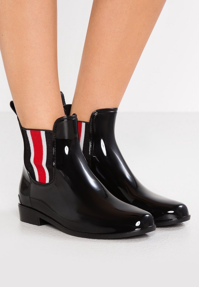 Bottes de cheville en caoutchouc noir avec des panneaux élastiques latéraux rayés rouges et blancs, dotées d'un petit talon carré et d'une finition brillante.