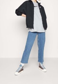 Svart lättjacka, grå t-shirt, blå rutiga jeans och flerfärgade högsålda sneakers. Avslappnad design och lös passform.