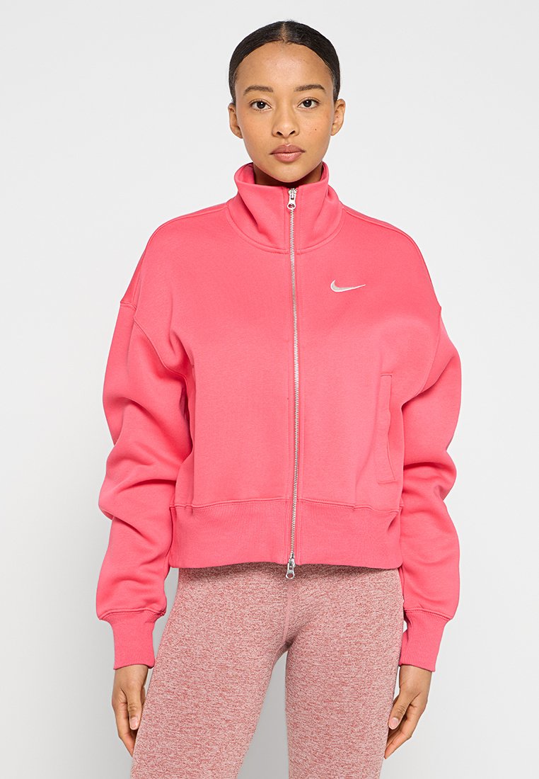 Różowa bluza rozpinana wykonana z miękkiego materiału, z wysokim kołnierzem i luźnym krojem, z małym białym logo Nike na klatce piersiowej.