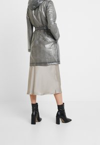 Šedá károvaná prošívaná bunda s kapucí a páskem v pase, nošená přes béžovou saténovou sukni a černé kotníkové boty na podpatku.