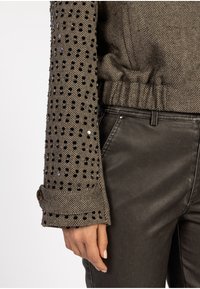 Braun kariertes Herringbone-Muster an den Ärmeln mit schwarzen Pailletten und Knopfmanschetten-Detail, kombiniert mit schwarzen strukturierten Hosen.