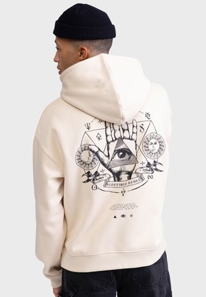 Beige hettegenser med et grafisk trykk på ryggen, som viser et øye, en sol og en hånd innen geometriske former. Stoffet er mykt og teksturert.