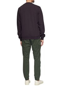 Donker paarse sweatshirt met een ronde hals, gecombineerd met groene cargo-broeken met elastische manchetten en zijzakken, afgemaakt met witte sneakers.