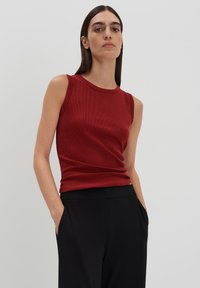 Top rosso a coste senza maniche con scollatura tonda, abbinato a pantaloni neri con design slim fit e texture sottile.
