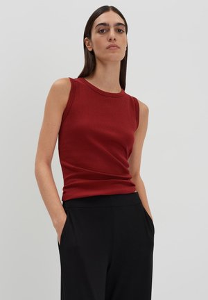 Red ribbed sleeveless top with a round neckline, paired with black trousers, featuring a slim fit design and subtle texture.