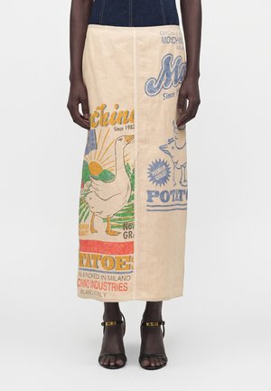 Bež maksik krilo s pisanim vintage potiskom gosi, sonca in besedila, nošeno s črnimi sandali z odprtim prstom in zlatimi napisnimi trakovi.