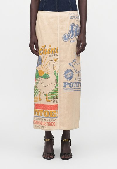 Jupe maxi beige avec un imprimé coloré de style vintage représentant des oies, le soleil et du texte, portée avec des talons ouverts noirs avec des brides à lettres dorées.