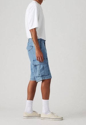 Jasnoniebieskie szorty cargo z denimu z wieloma kieszeniami, płaskim przodem i luźnym krojem, zestawione z białą koszulką i beżowymi półbutami.