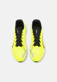Zapatillas deportivas amarillas con una parte superior de malla transpirable, cordones negros y una suela texturizada. Presentan un logotipo plateado en el costado.