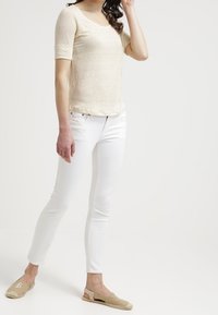 Jasno beżowa dopasowana koszulka z krótkim rękawem, zestawiona z białymi dopasowanymi dżinsami i beżowymi espadrylami, prezentująca gładką teksturę i codzienny styl.