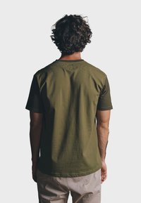 Camiseta de algodón verde oliva de manga corta con cuello redondo, corte recto y textura suave, vista desde la espalda.