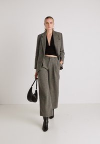 Blazer cinza com padrão em espinha de peixe e calças largas combinando, acompanhados por um top crop preto e botas pretas de cano curto. Bolsa preta.