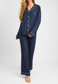 Granatowy zestaw piżamowy wykonany z miękkiej tkaniny; koszula zapinana na guziki z białym wykończeniem i jedną kieszonką na piersi, w komplecie z luźnymi spodniami.