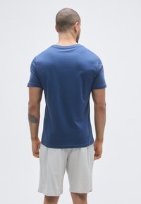 T-shirt bleu à manches courtes en tissu lisse, coupe ajustée, avec un col rond, associé à un short gris clair.